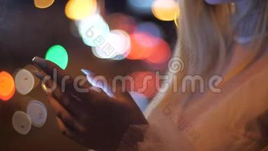 晚上在城市里用智能手机特写金发女人的手。 在城市街道的智能手机上输入信息